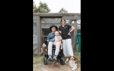 A man using an electric wheelchair and his baby Milo on his lap with his support worker and two fluffy border collie dogs